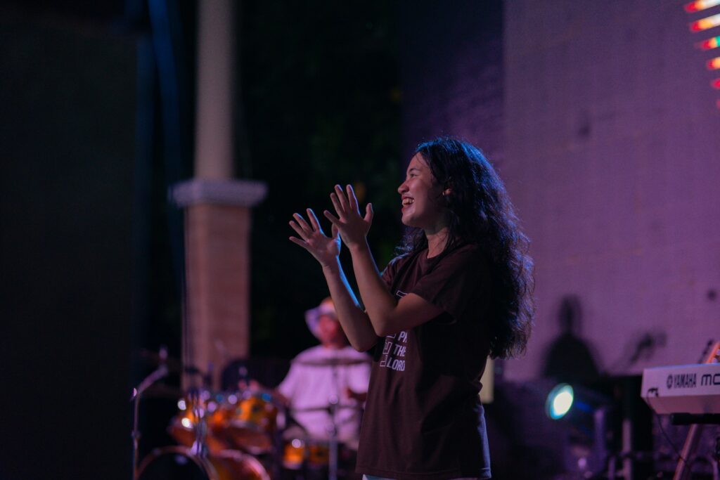 Photo by Ziph A woman standing on a stage with her hands in the air